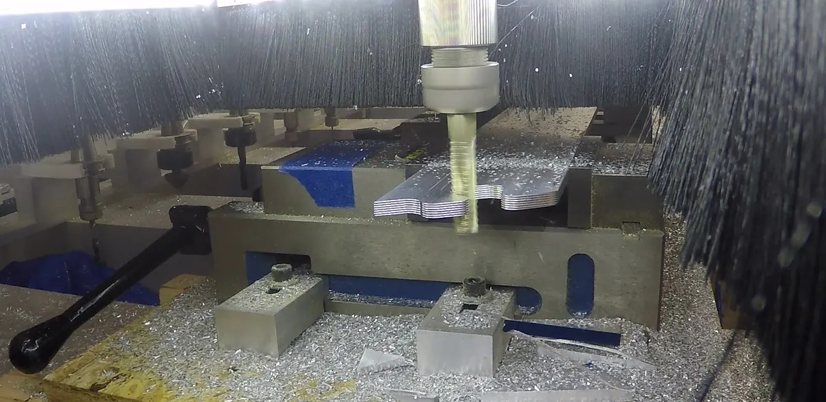 End mill cutting stacked aluminum Z-channel held in a machine vise, with chips across the table