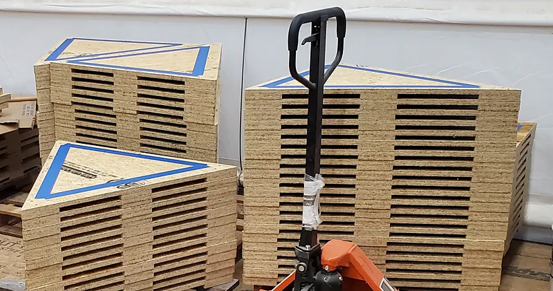 Stacks of CNC-cut triangular dome panels marked with layout lines, on pallets in the shop