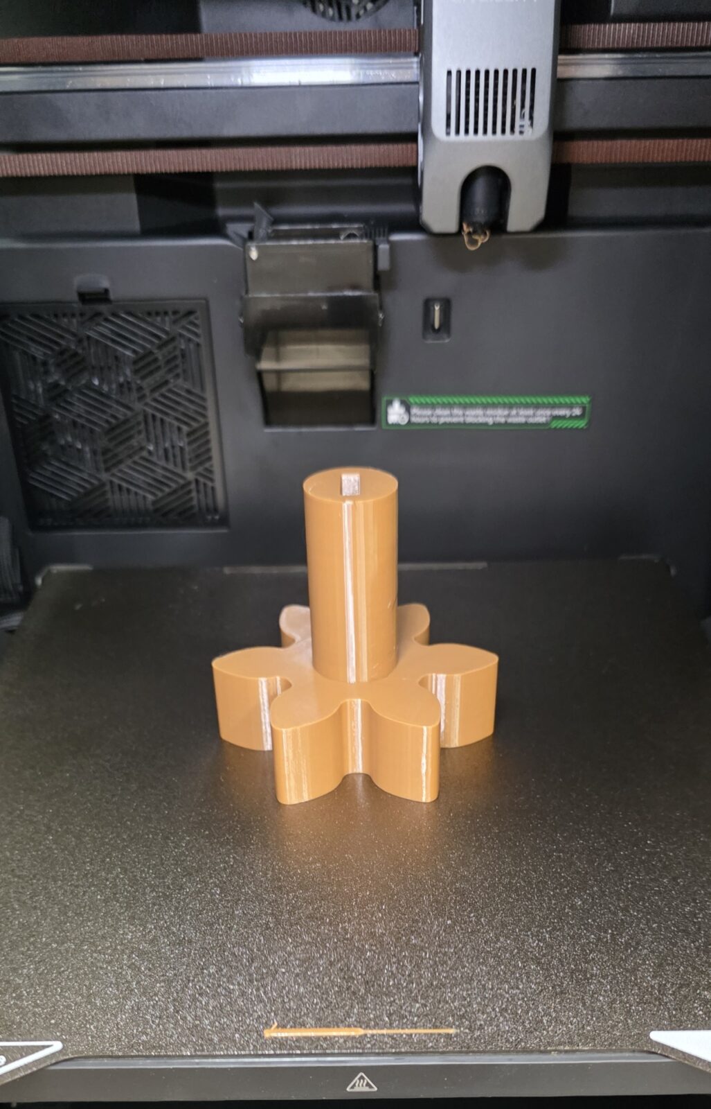 The same star-shaped knob 3D printed in tan filament on the printer bed